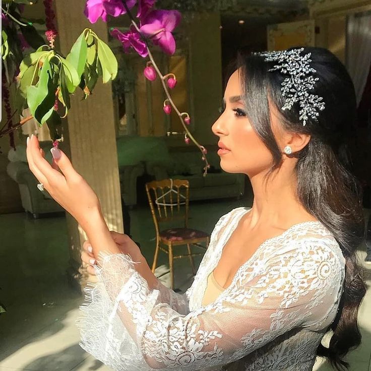 a woman in a white dress is holding a branch with purple flowers on it and wearing a tiara