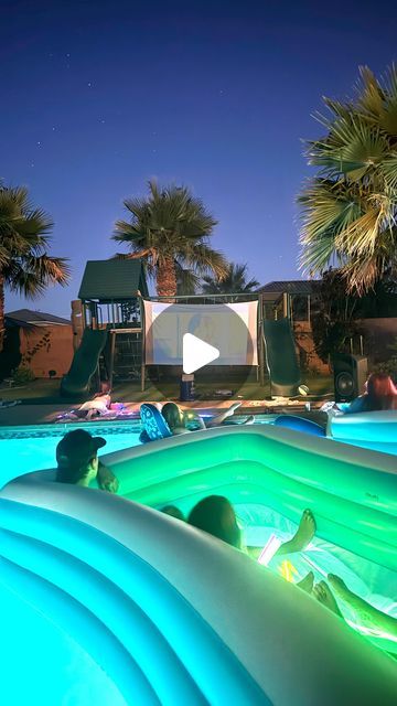 an inflatable pool is lit up at night with palm trees and chairs around it