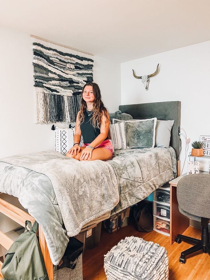 a woman sitting on top of a bed in a room with wooden floors and white walls