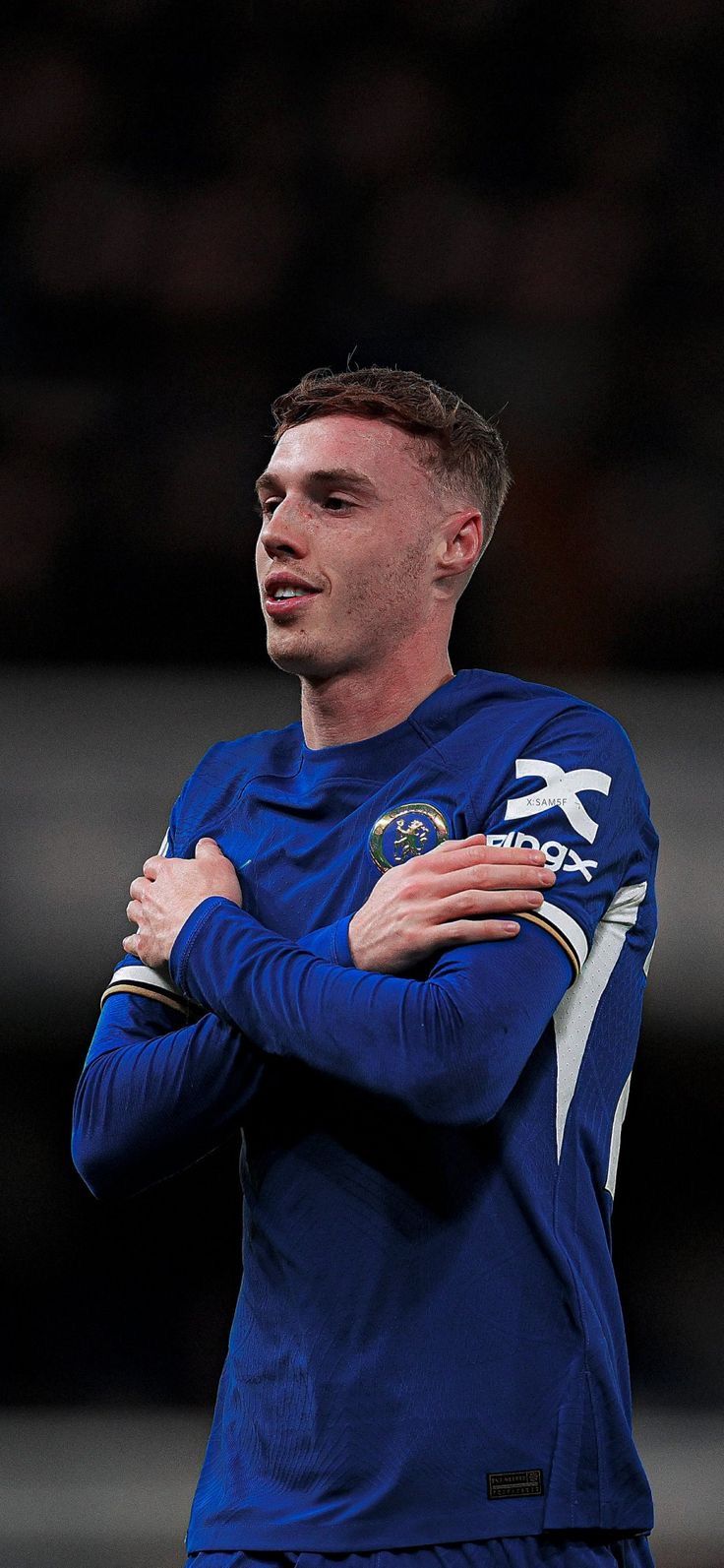 a soccer player with his arms crossed looking to the side while wearing a blue uniform