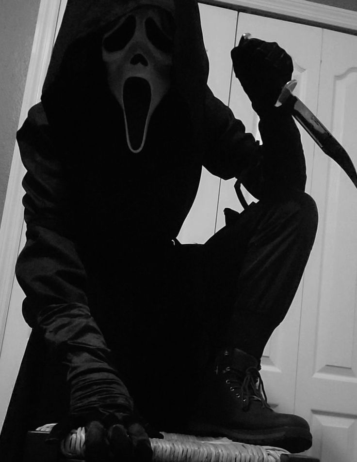 a person in a black outfit holding a knife and sitting on a stool with his mouth open