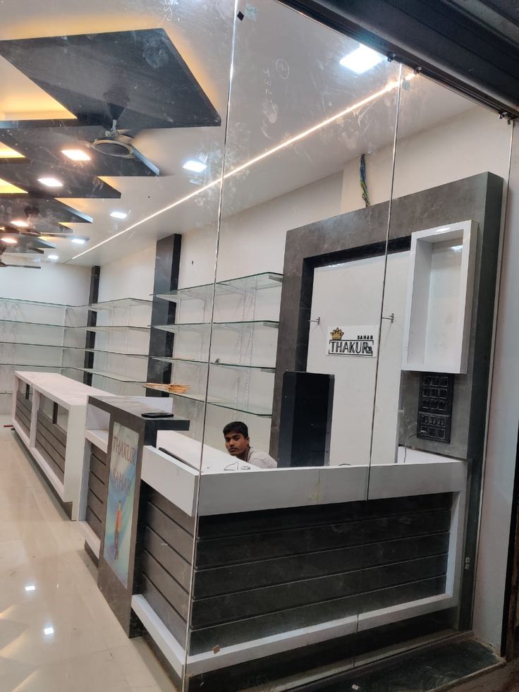 a man is sitting at the front desk of a store with glass walls and shelving