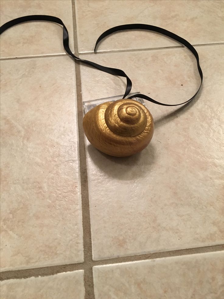 a small gold shell on a black cord laying on the floor next to a tile floor