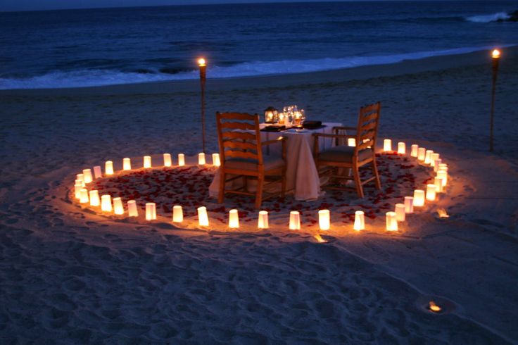 a dinner table set up on the beach with candles in the shape of a circle