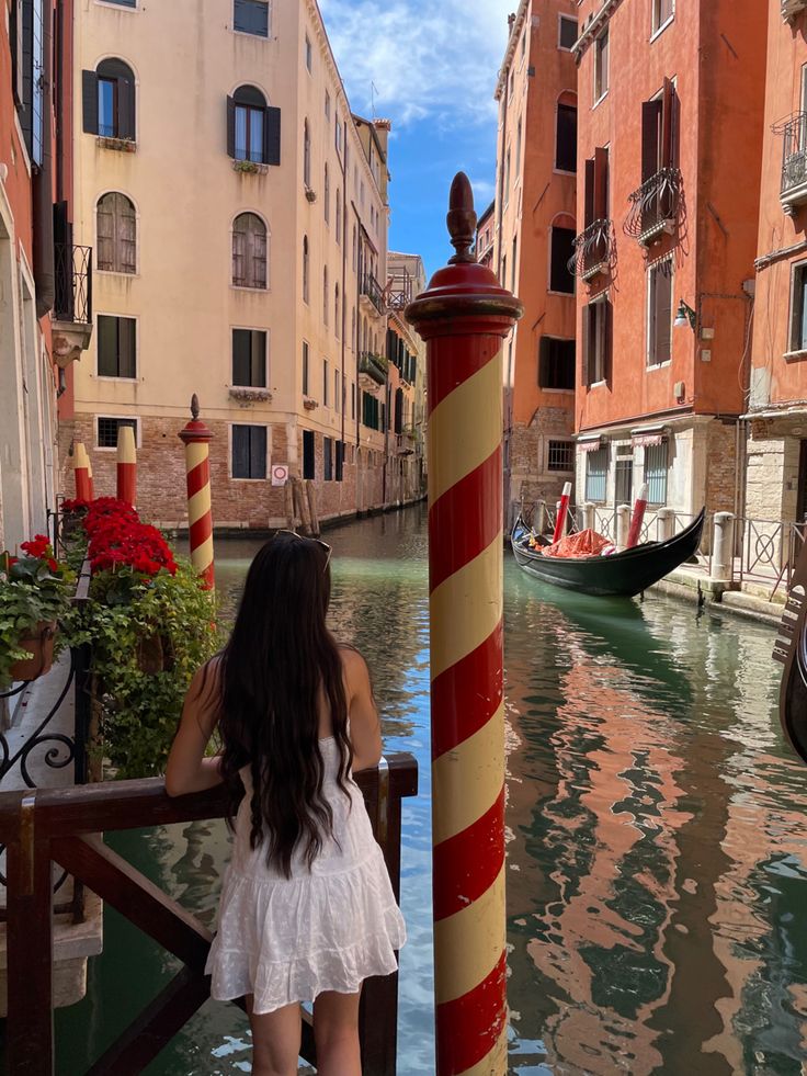 a woman standing on a bridge next to a canal with gondolas in the background