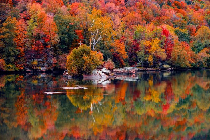 a lake surrounded by colorful trees in the middle of fall with water reflecting it's colors