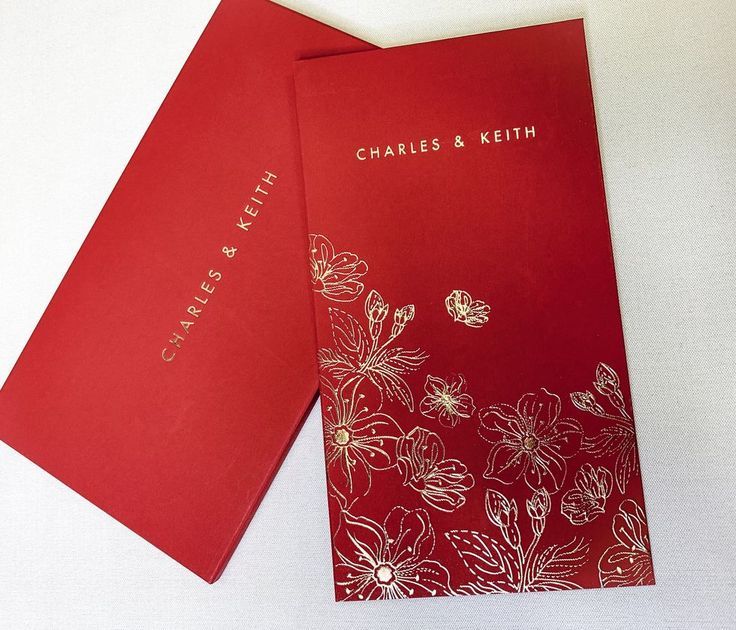 two red wedding cards with gold foil flowers on the front and back, sitting next to each other