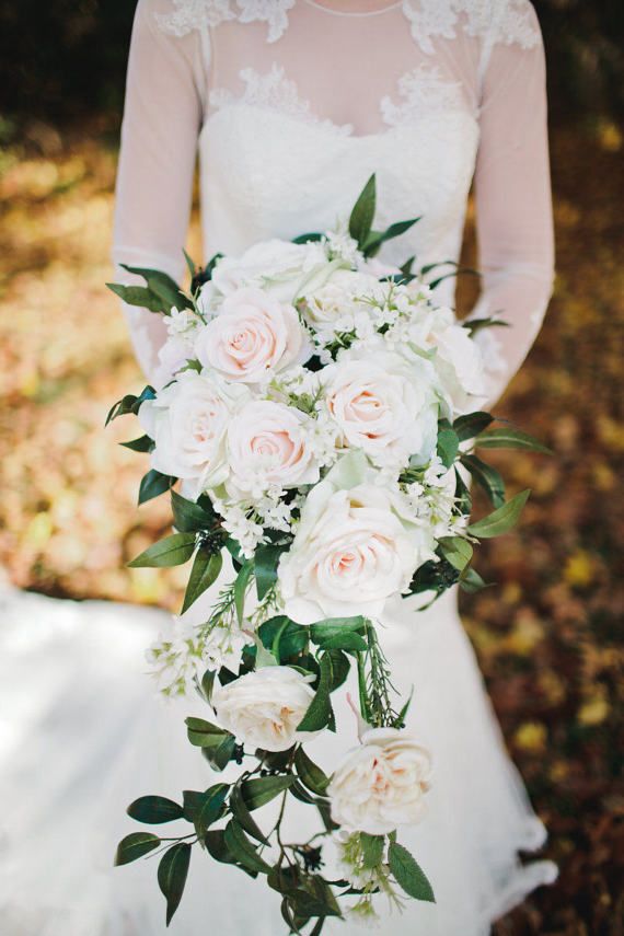 a bridal holding a bouquet of white roses and greenery in her hands,