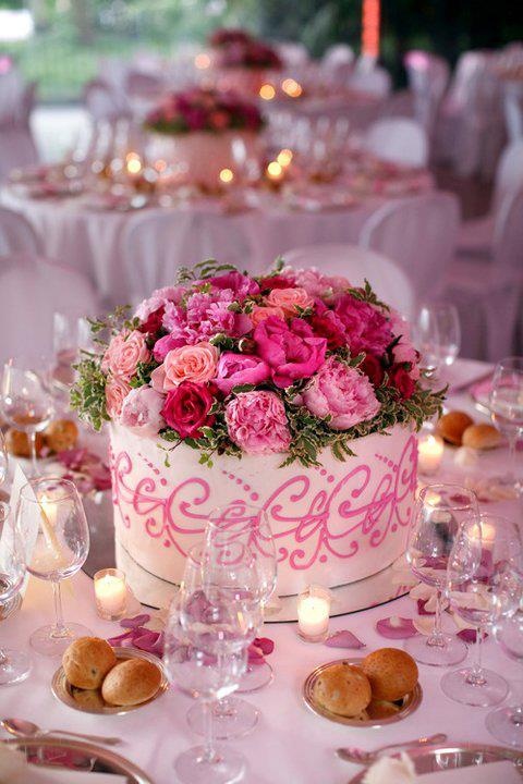 a wedding cake decorated with pink flowers and greenery on a table set for a formal function