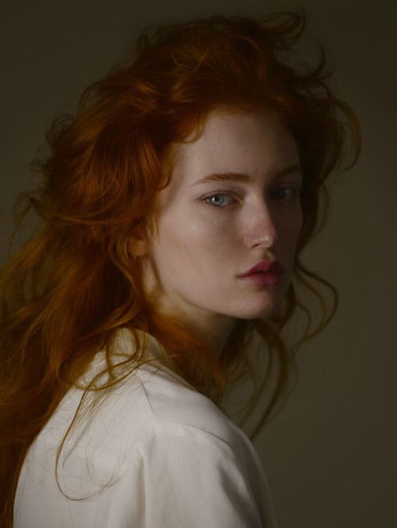 a woman with red hair and blue eyes is looking at the camera while wearing a white shirt