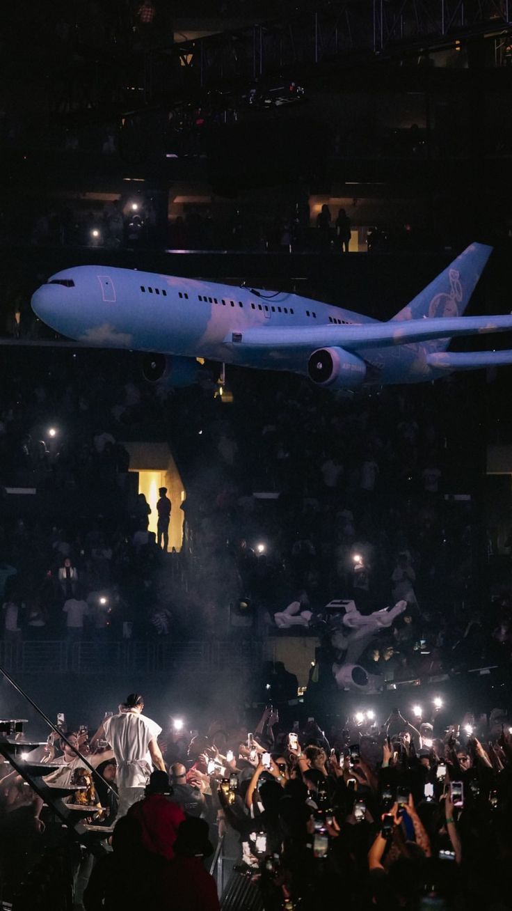 a large airplane flying over a crowd of people at an event in front of a stage