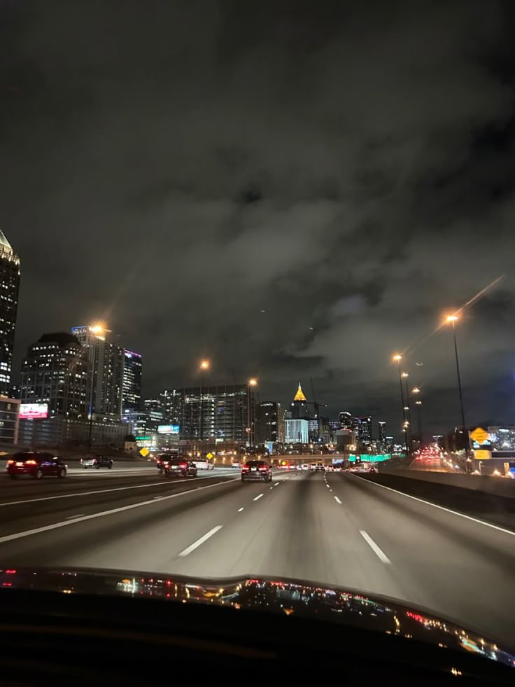 the city lights shine brightly in the distance as cars drive down the highway at night