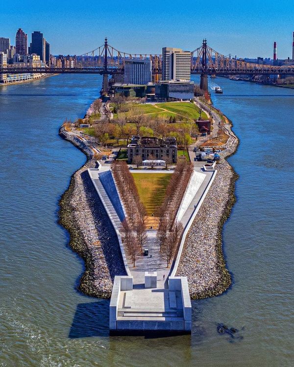 an island in the middle of a body of water with a bridge and buildings in the background