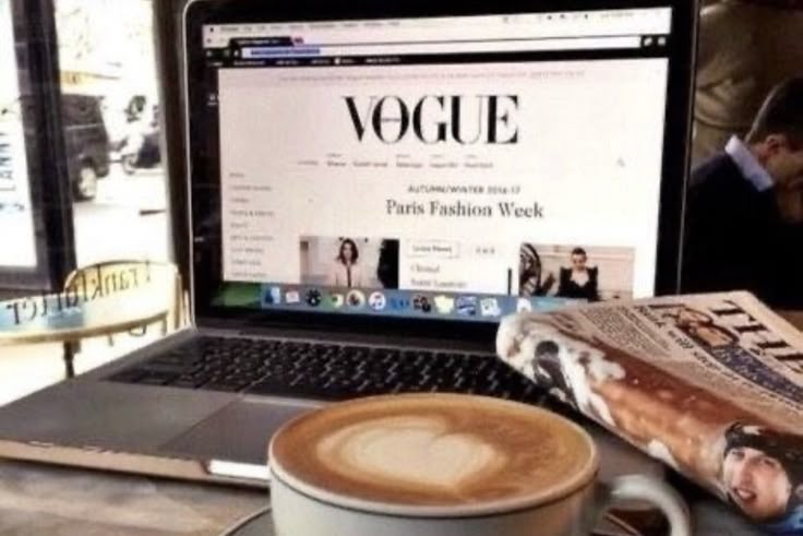 a laptop computer sitting on top of a table next to a cup of coffee and magazine