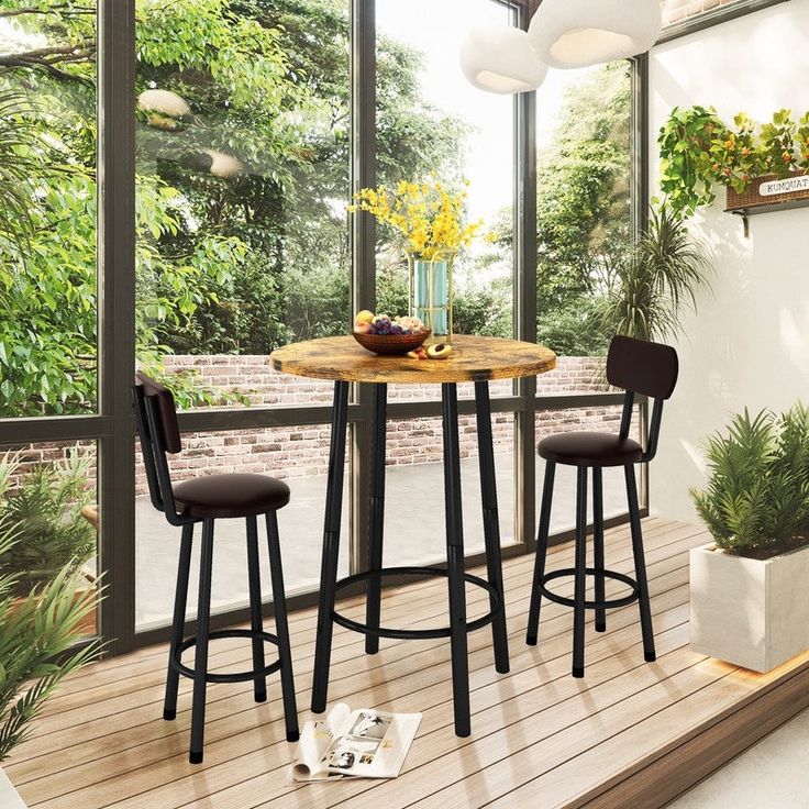 a small table with two stools in front of a large window and potted plants