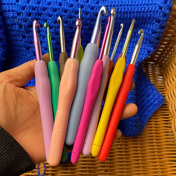 a person holding a bunch of colorful pens in their palm next to a wicker basket