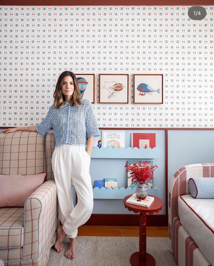 a woman standing next to a couch in a room with blue and white wallpaper