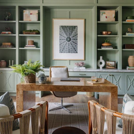 an office with green walls and wicker chairs in front of a wooden table surrounded by bookshelves