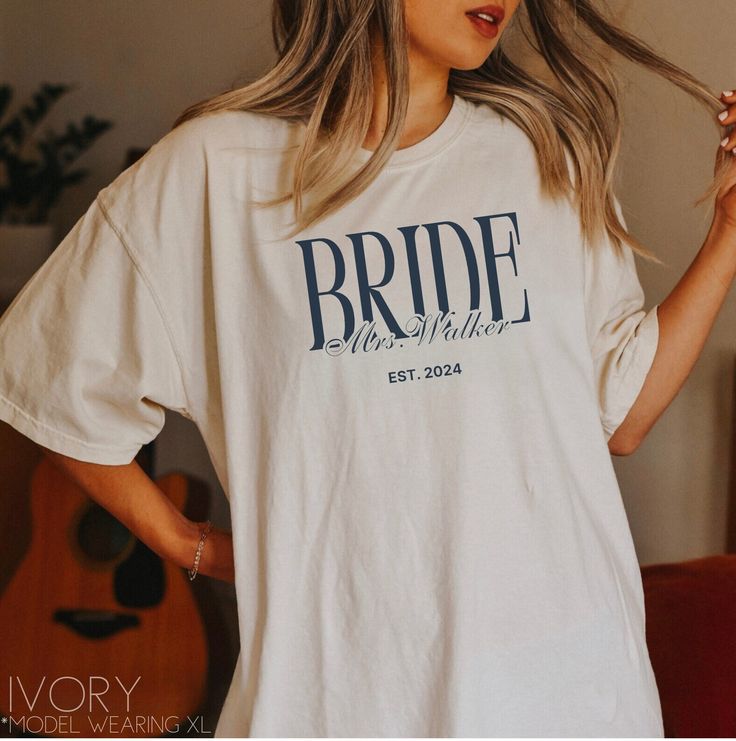 a woman wearing a white t - shirt with the word bride printed on it, standing in front of a guitar