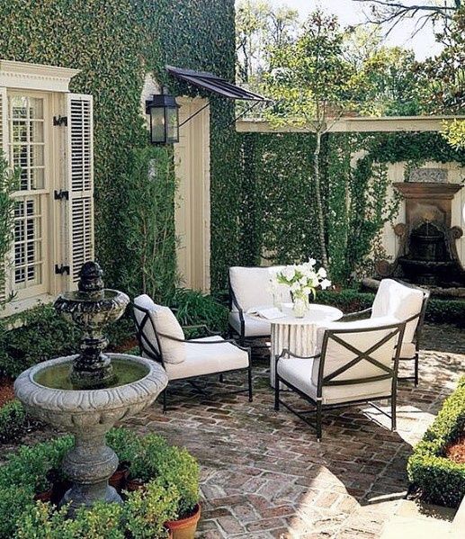 an outdoor patio with chairs, table and water fountain in the center surrounded by greenery