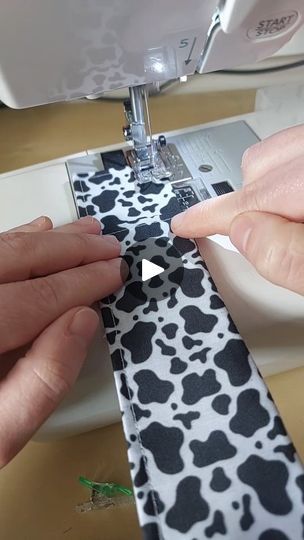 two hands are using a sewing machine to sew on a black and white tie