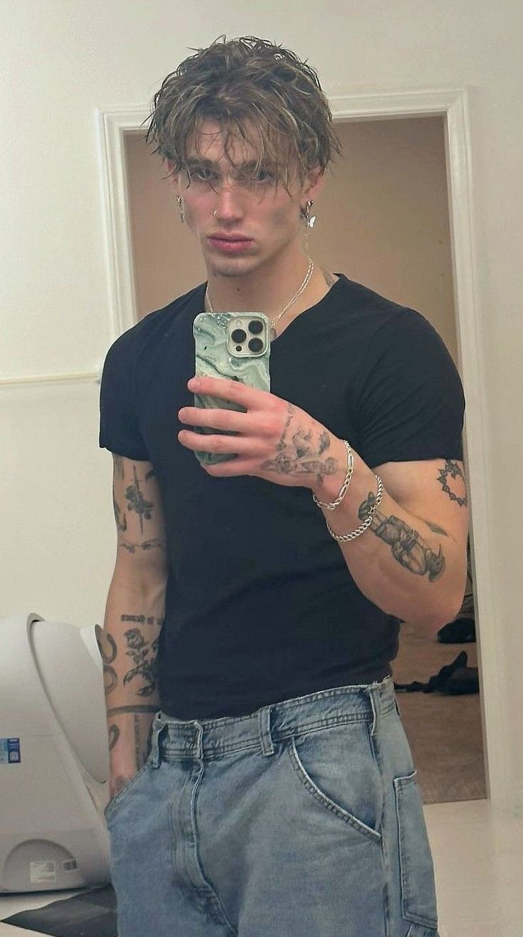 a man taking a selfie with his cell phone in front of him and tattoos on his arms