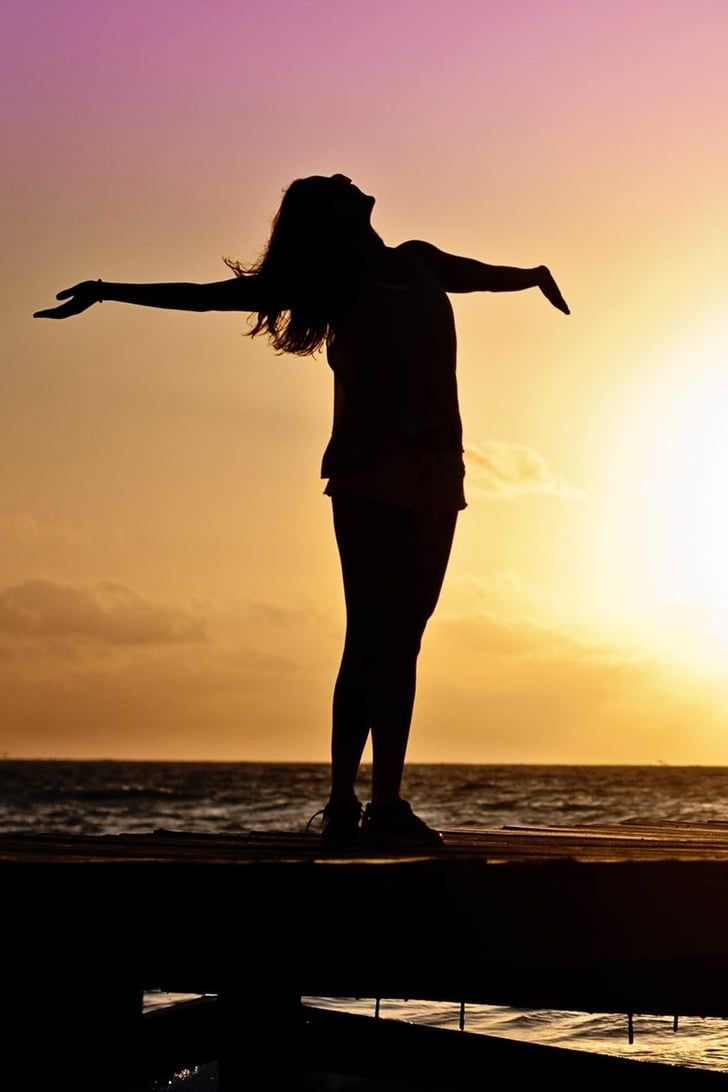 a woman standing on top of a pier next to the ocean at sun set with her arms outstretched