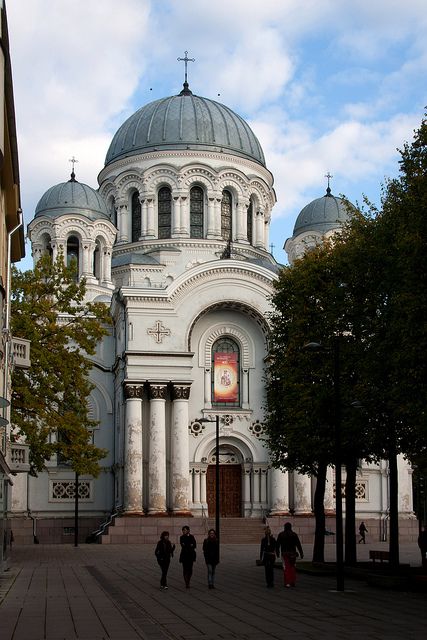 people walking in front of a large white building with two domes on it's sides