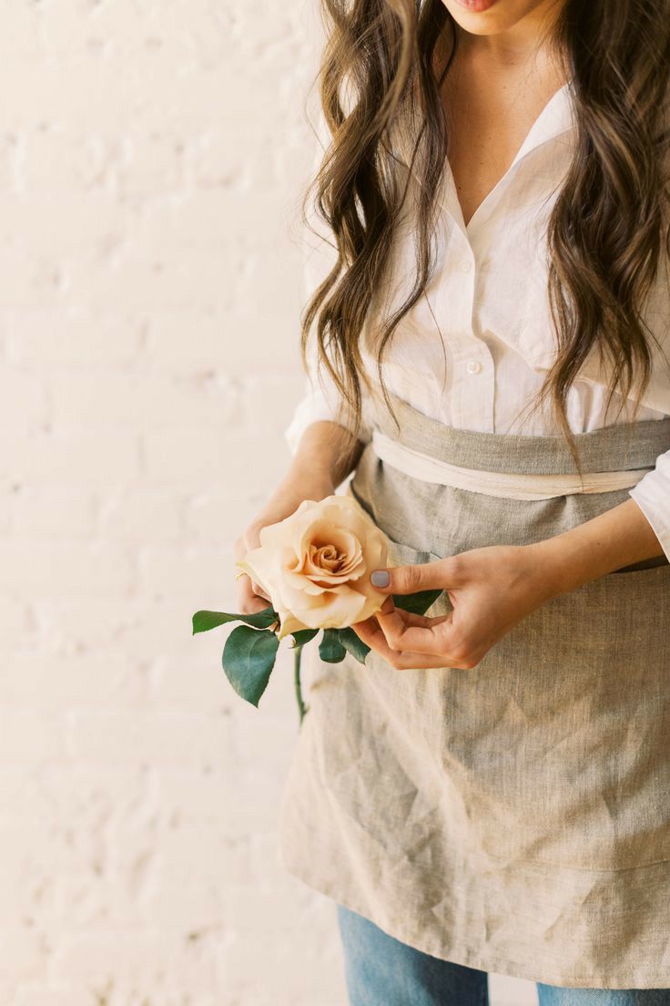 a woman is holding a flower in her right hand and wearing an apron on the other side