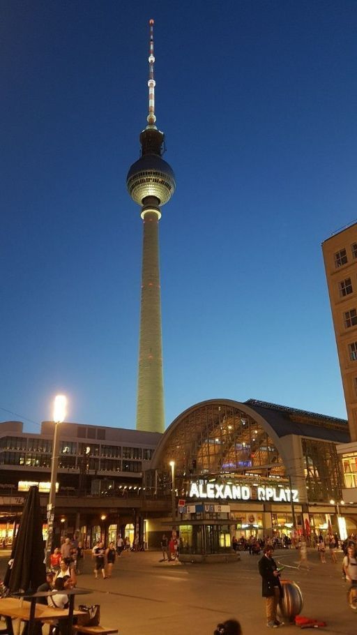 people sitting on benches in front of a tall building with a television tower in the background