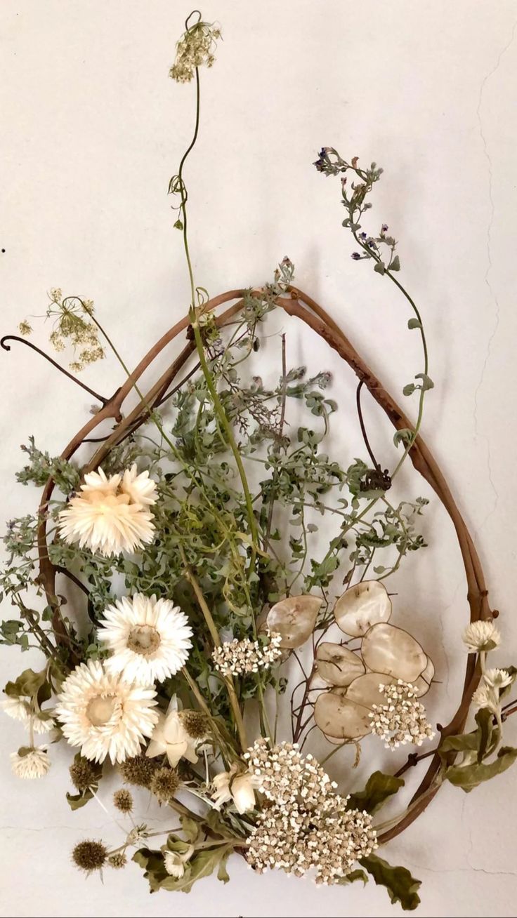 an arrangement of flowers arranged in a circle on a white wall with vines and leaves