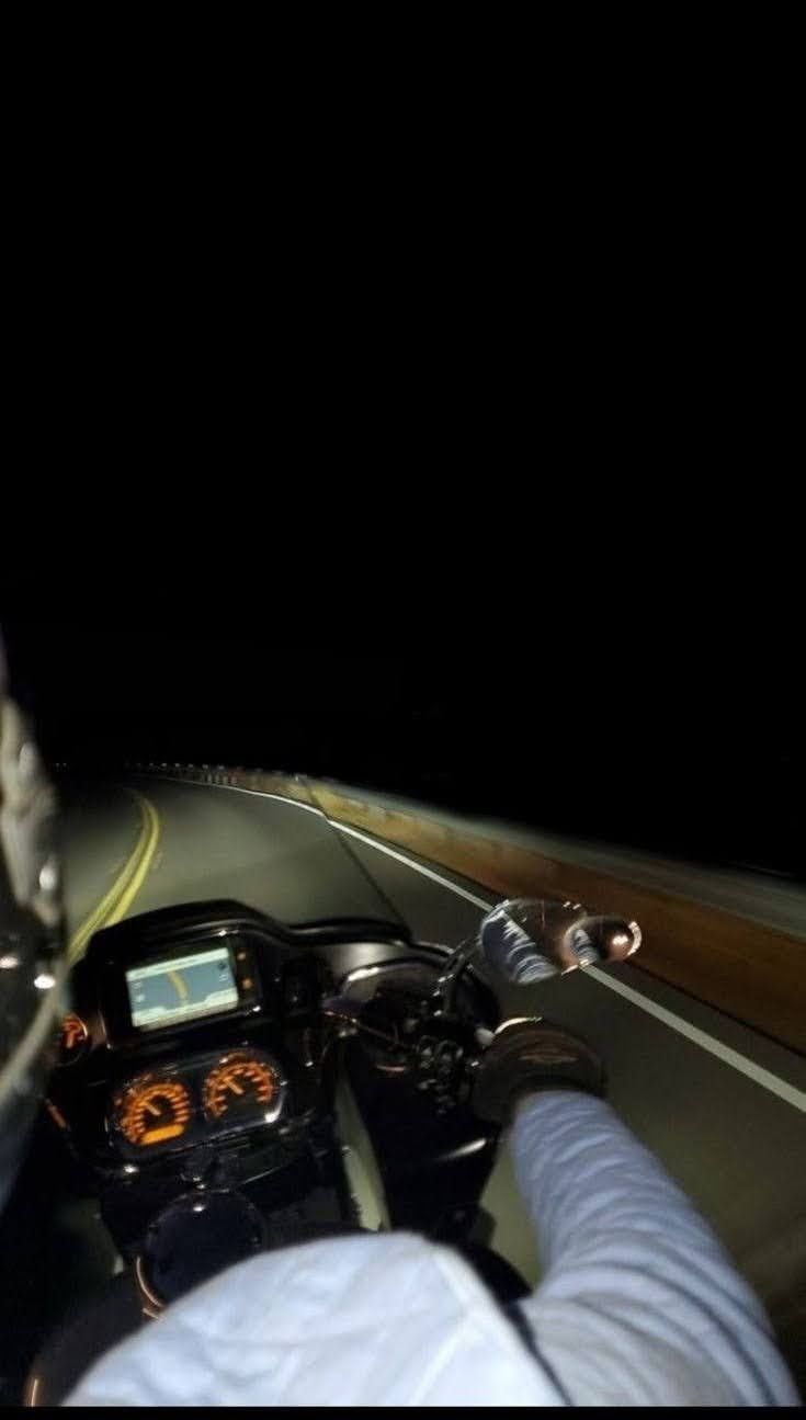 a person riding on the back of a motorcycle down a curvy road at night