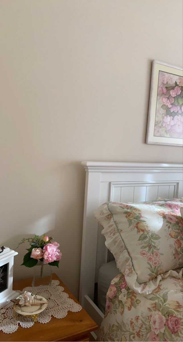 a bed with pink flowers on it next to a small table and pictures above the headboard