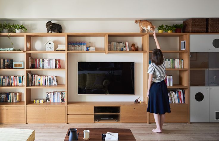 a woman holding a cat up in front of a large television set with bookshelves