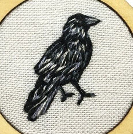 a black bird sitting on top of a white and gold circle embroidered onto a piece of cloth