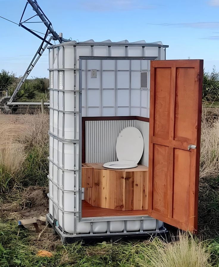 an outhouse with a toilet in it sitting on top of some grass and dirt