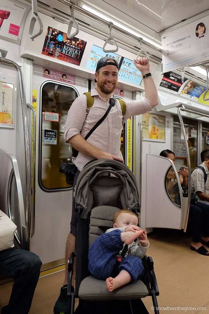 a man standing next to a baby in a stroller on a train with other people