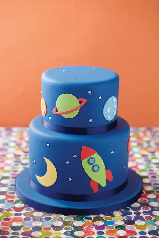 a three tiered cake decorated with rockets and planets on it's blue icing