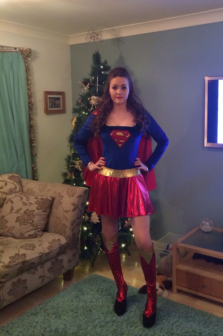 a woman in a superman costume standing next to a christmas tree with her hands on her hips