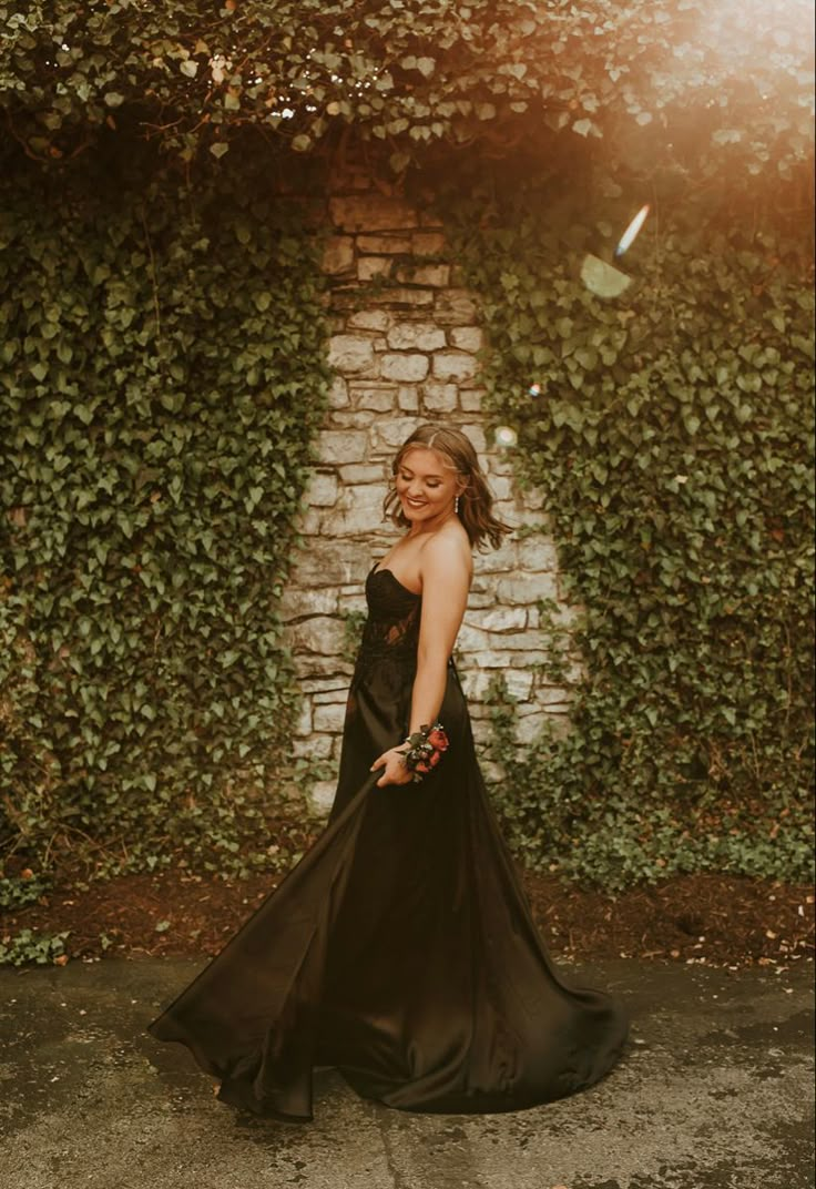 a woman standing in front of a brick wall wearing a long black dress and heels