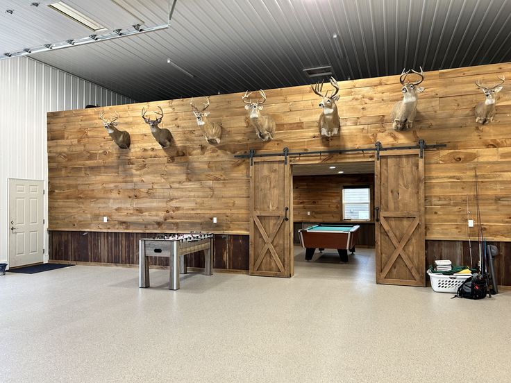 a room with several deer heads mounted to the wall and two pool tables in front of it