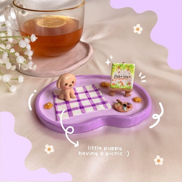 a baby doll is sitting on a purple tray next to a cup of tea