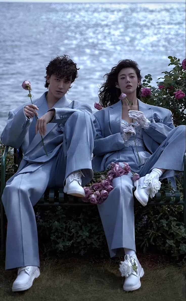 two people sitting on a bench next to the ocean with flowers in their lapels