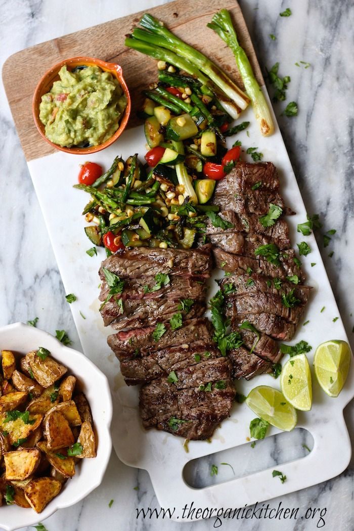 steak, potatoes and asparagus on a cutting board next to a bowl of guacamole