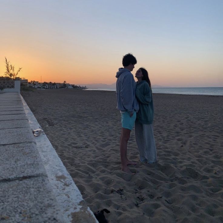 two people standing on the beach at sunset