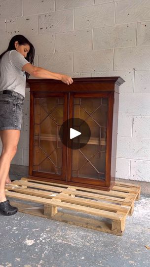 a woman standing next to a wooden cabinet on top of pallet boards with the door open