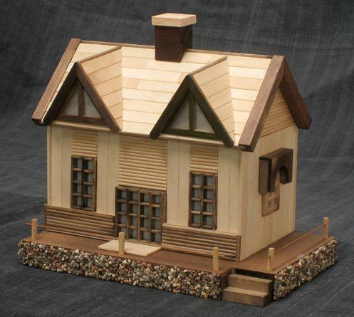 a small model house sitting on top of a stone base with windows and shutters