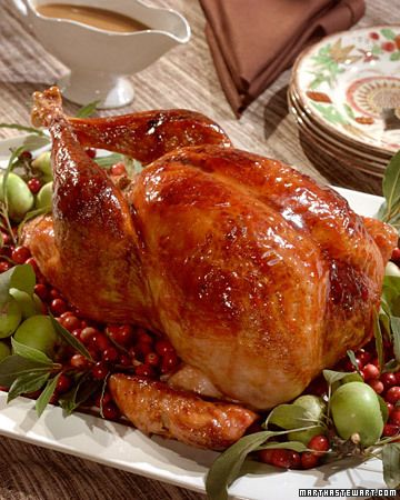 a roasted turkey on a platter with berries and green olives next to a cup of coffee