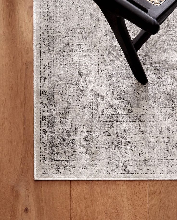 a black chair sitting on top of a wooden floor next to a white and gray rug