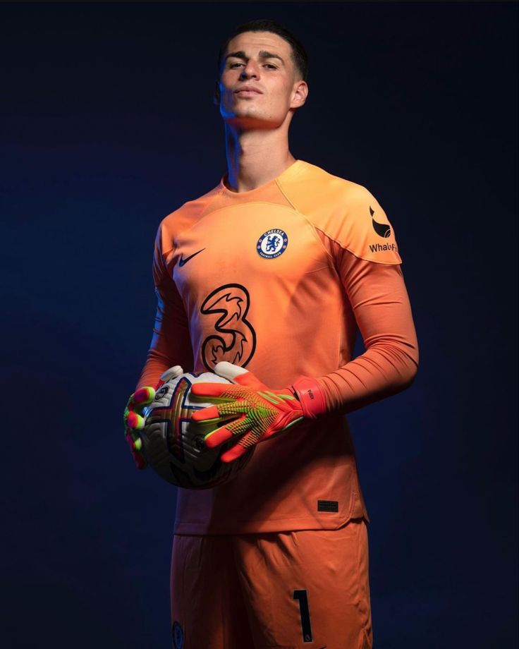 a man in an orange goalkeeper's uniform holding a soccer ball and mitts